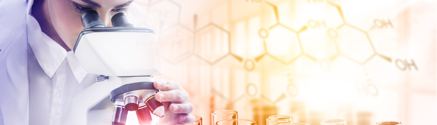 Student in white lab gear peering down a microscope, in front of a backdrop of beakers and molecule